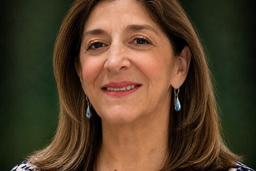 Audry Portrait of a smiling middle-aged woman with shoulder-length brown hair, wearing blue teardrop earrings.