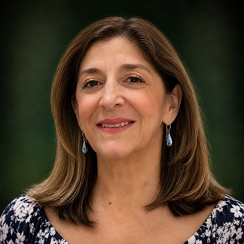 Audry Portrait of a smiling middle-aged woman with shoulder-length brown hair, wearing blue teardrop earrings.